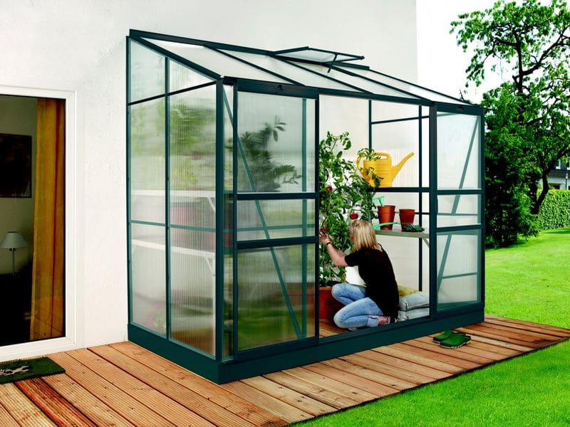 Polykarbonátový skleník ke zdi Vitavia IDA se ženou pečující o květiny