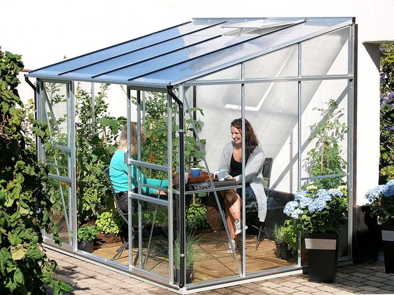 Skleník u zdi domu Vitavia IDA s posezením a dvěma ženami u kulatého stolku