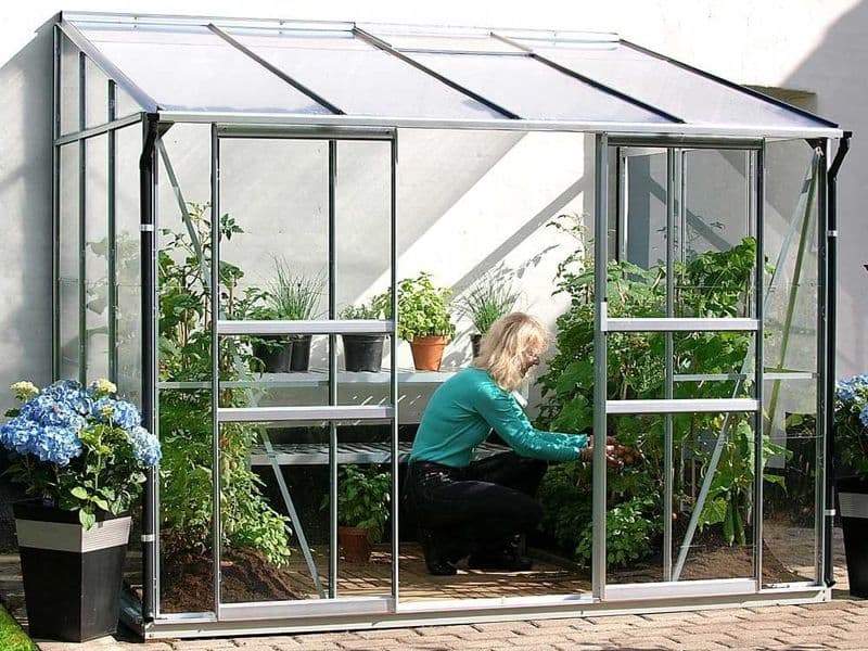 Skleník ke zdi Vitavia IDA se ženou pečující o výsadbu